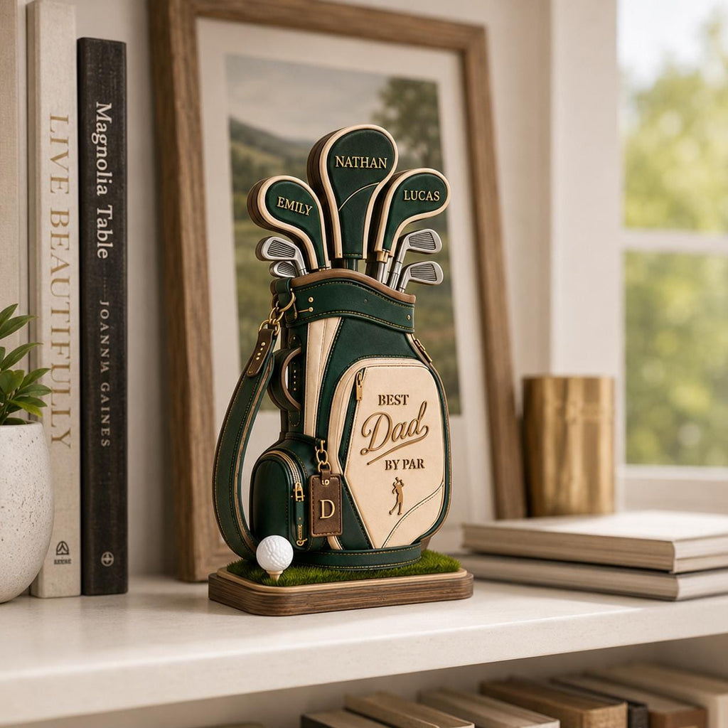 May include: A decorative golf bag figurine in green and tan, with the words "Best Dad by Par." The bag holds golf clubs with personalized name tags. A golf ball sits on a small patch of green grass. The figurine is on a wooden base.
