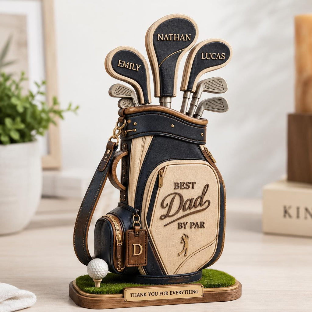 May include: A golf bag-shaped decorative item with the words "Best Dad by Par" and "Thank You For Everything". The bag is black and beige with golf clubs labeled "Emily", "Nathan", and "Lucas". A golf ball sits on a tee in front.
