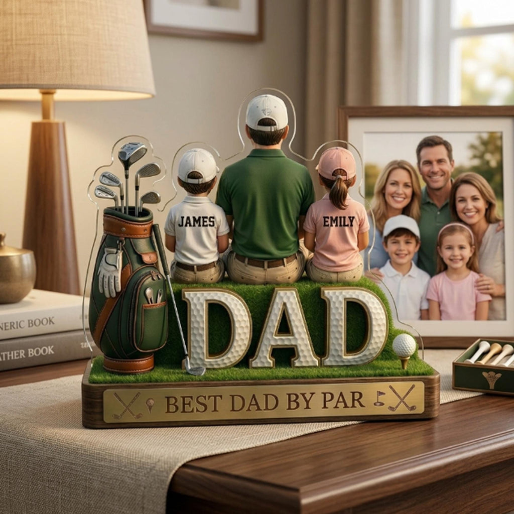 May include: A clear acrylic golf-themed display featuring a family of four, with the word "DAD" in large letters. The display includes a golf bag, golf clubs, and the text "BEST DAD BY PAR". A framed family photo is in the background.