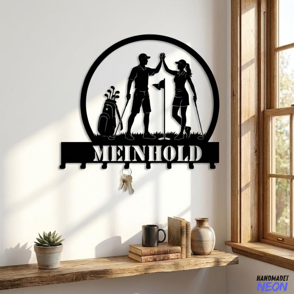 May include: Black metal key holder featuring a golf-themed design with two figures giving a high-five. The word "MEINHOLD" is displayed below the figures. Includes key hooks and a circular frame. A golf bag and flag are also visible.