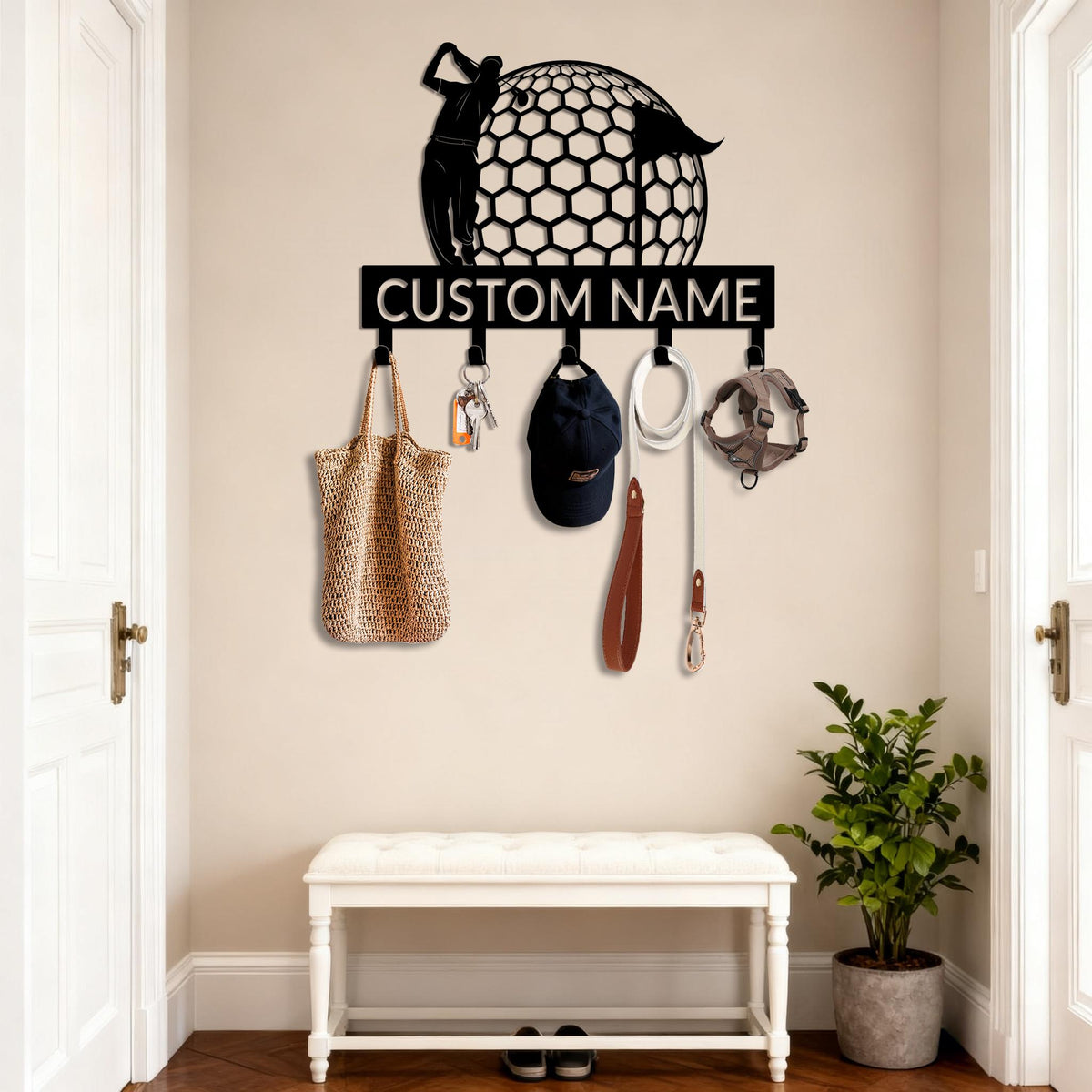 May include: Black metal wall-mounted key holder with a golf theme. The design features a golfer and a golf ball with a honeycomb pattern. The text "CUSTOM NAME" is displayed below the golf ball. Various items hang from the hooks, including a tote bag, keys, a cap, and a dog leash.
