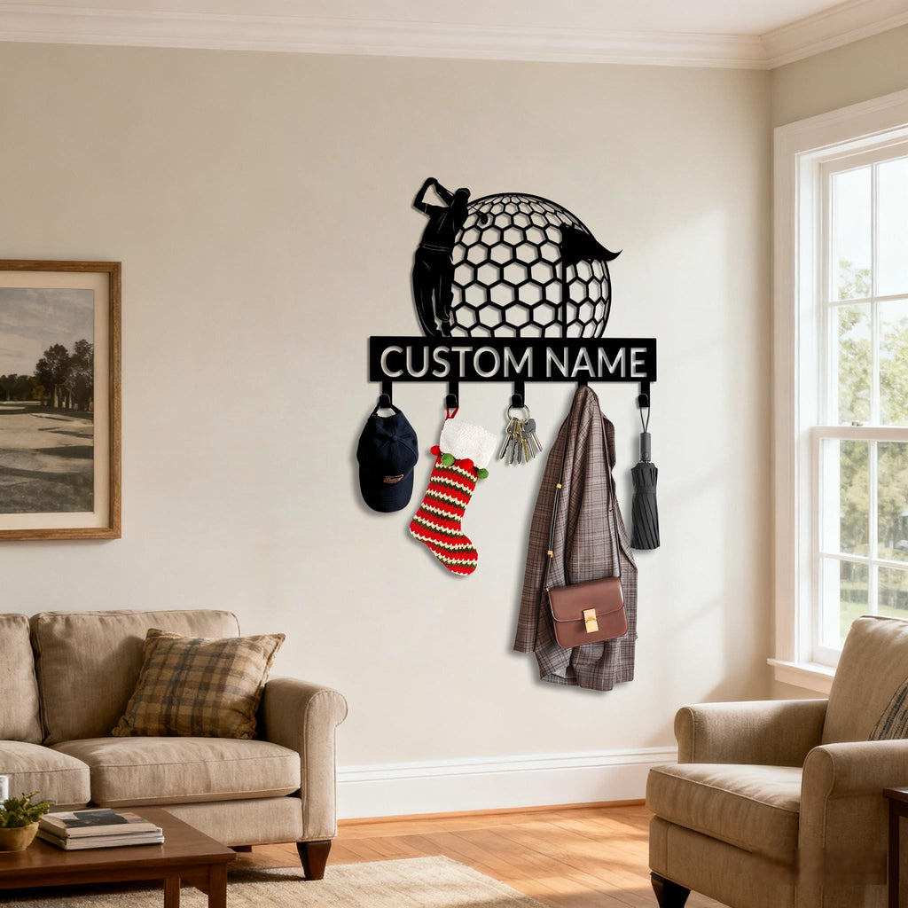 May include: Black metal golf-themed wall-mounted coat rack with hooks. Features a golfer silhouette, a golf ball design, and the text "CUSTOM NAME". Includes a baseball cap, a Christmas stocking, keys, a coat, a purse, and an umbrella.
