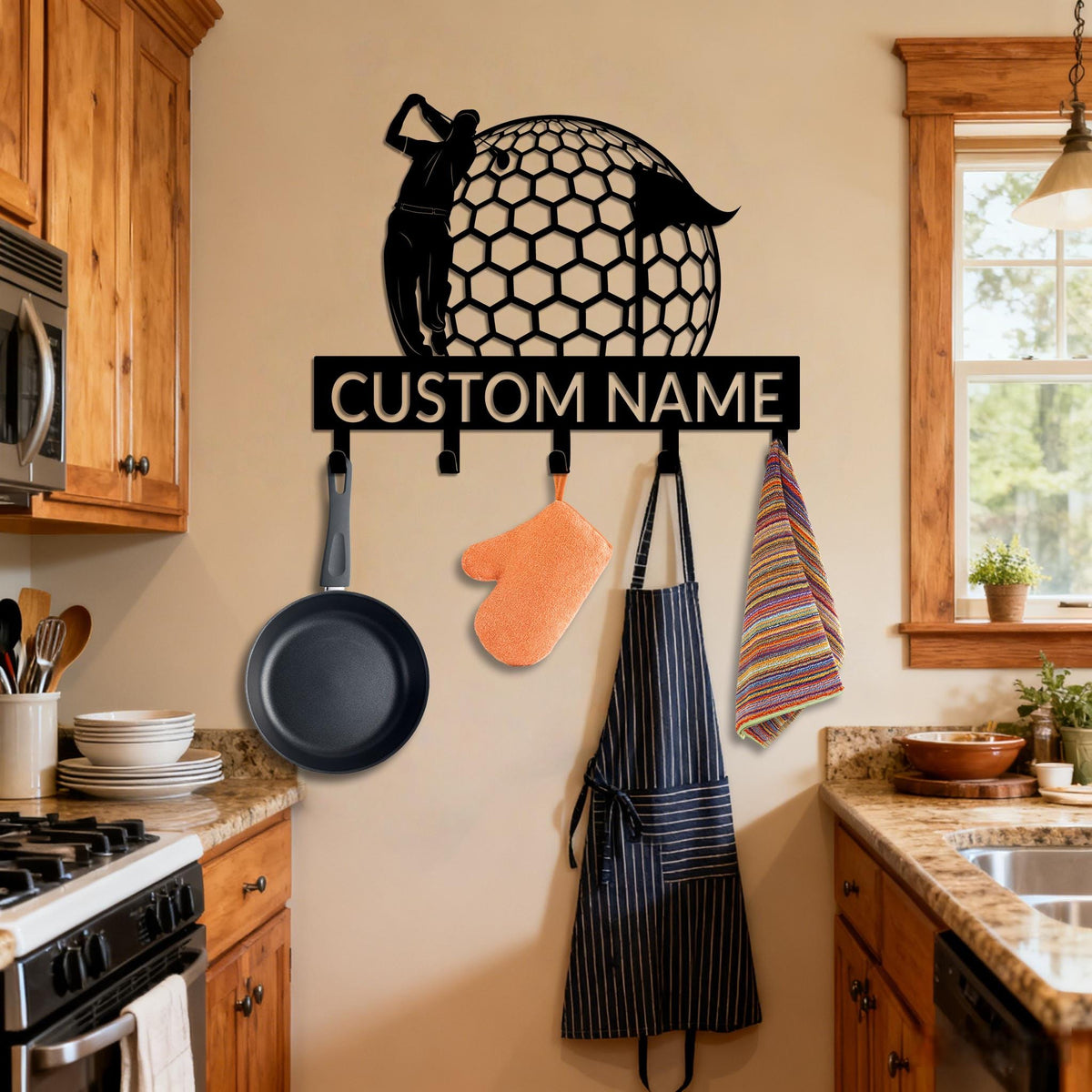 May include: Black metal wall-mounted kitchen rack featuring a golfer silhouette and a golf ball design. The rack has hooks for hanging kitchen items, with the text "CUSTOM NAME" across the top. A frying pan, oven mitt, apron, and towel are hanging from the hooks.