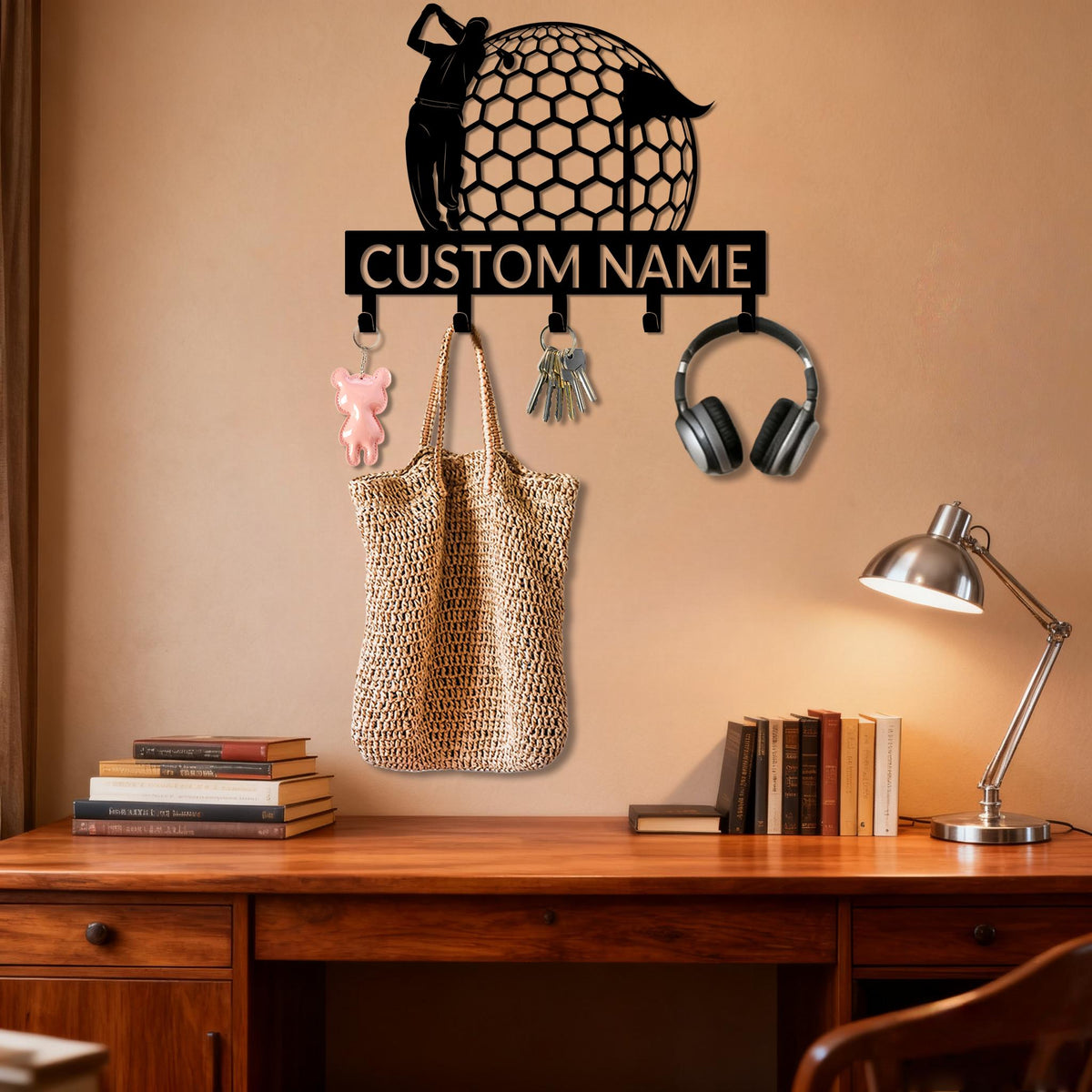 May include: A black metal wall-mounted key holder featuring a golf-themed design with a golfer silhouette and a honeycomb-patterned golf ball. The key holder has hooks for keys, a tote bag, and headphones. The text "CUSTOM NAME" is displayed.