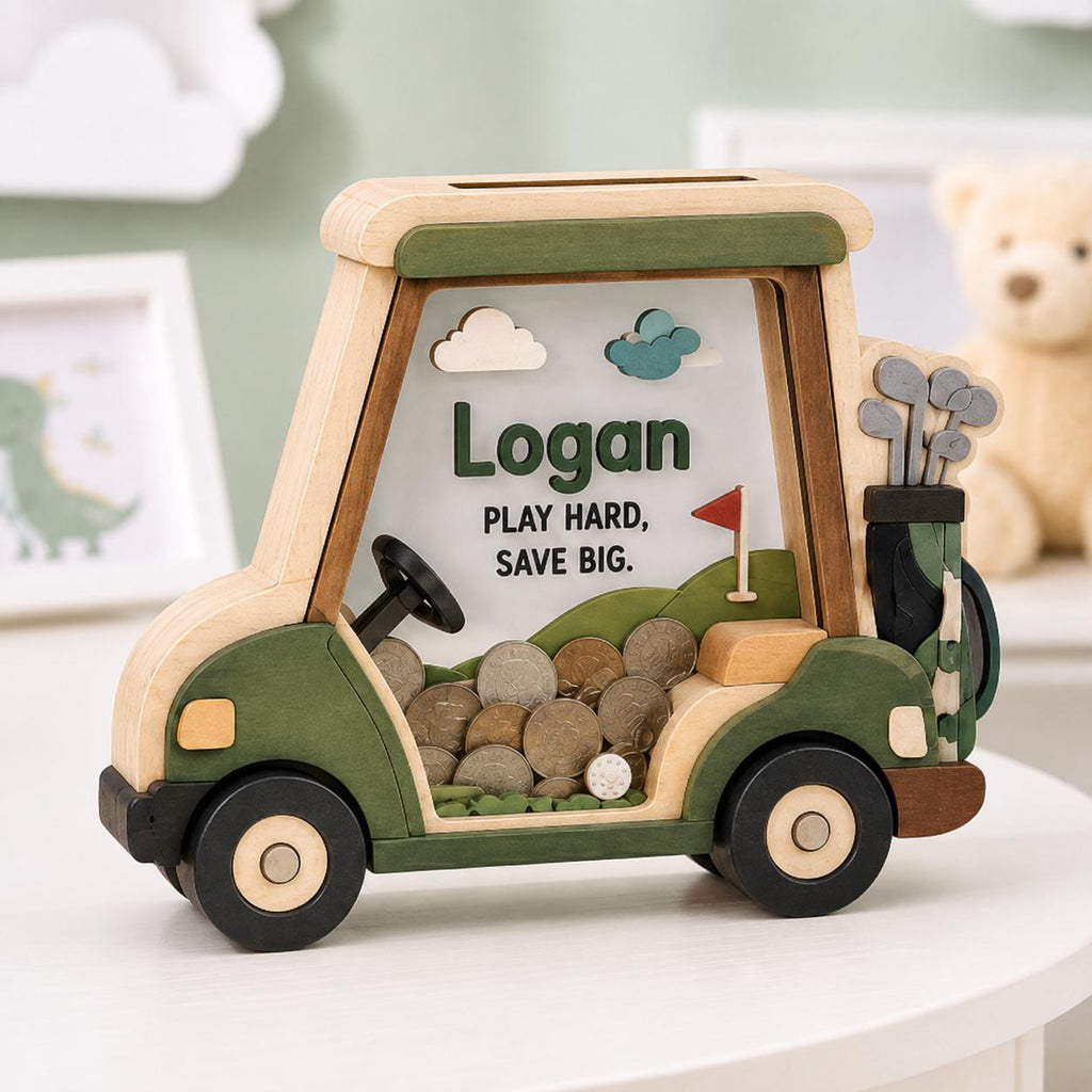 May include: A wooden golf cart shaped piggy bank with green and natural wood tones. The clear front panel displays the name Logan and the text PLAY HARD, SAVE BIG. A golf bag with clubs is attached to the back, and the interior contains coins.