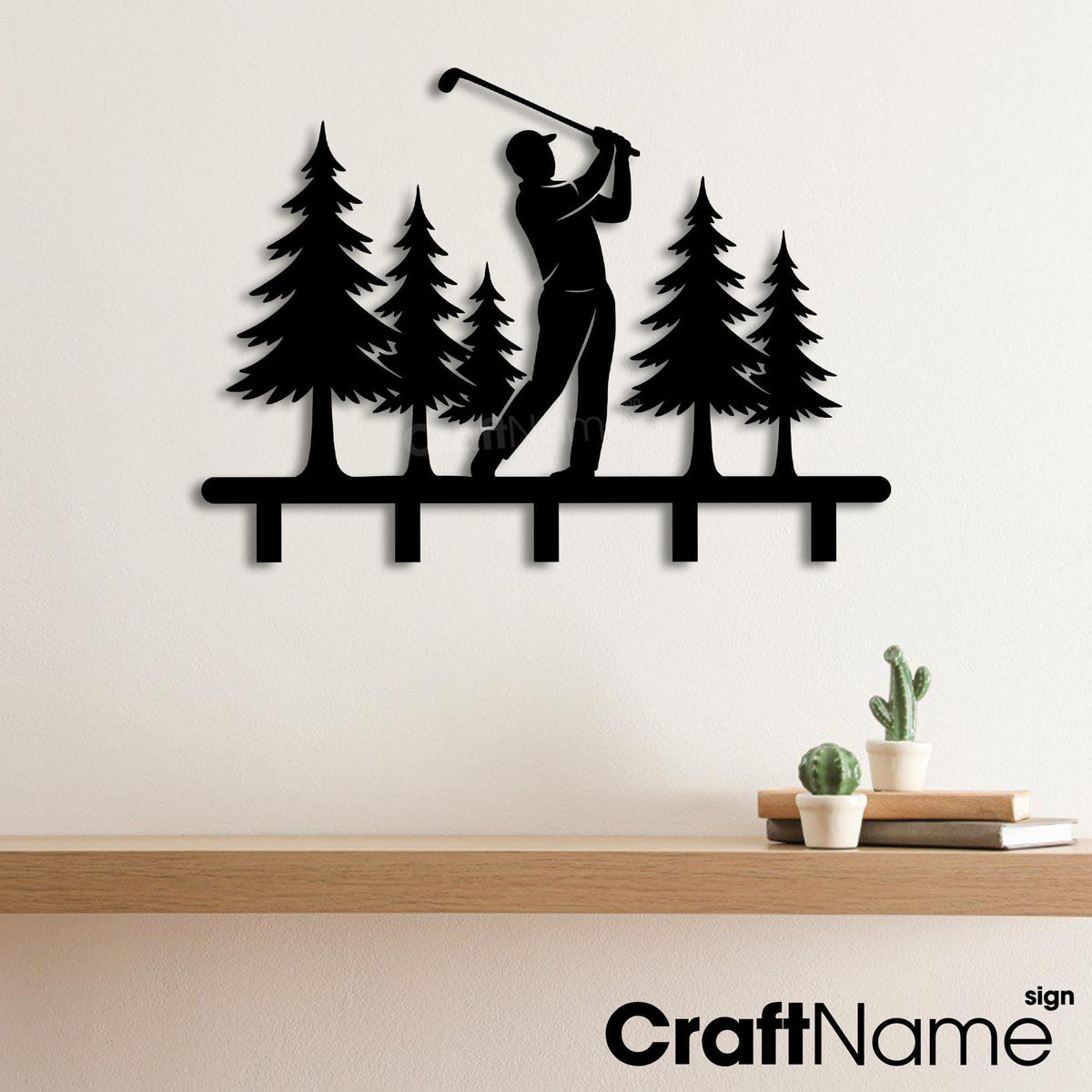 May include: A black metal wall-mounted rack featuring a silhouette of a golfer swinging a club amidst five pine trees. The design includes five downward-facing hooks integrated into the base, creating a functional piece for hanging items.