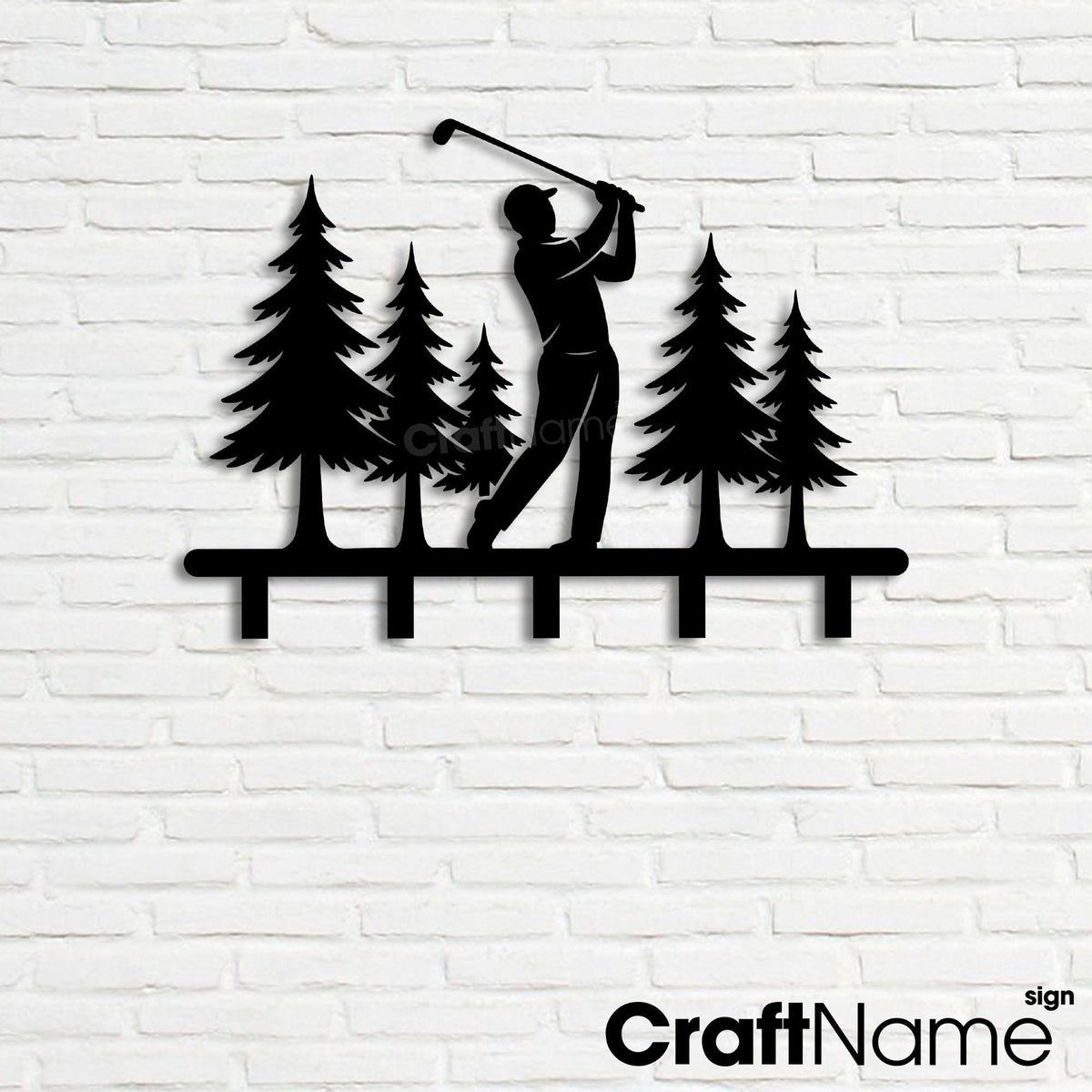 May include: A black metal wall-mounted hook rack featuring a silhouette of a golfer swinging a club amidst a forest of five pine trees. The design includes a horizontal base bar with five downward-facing hooks for hanging items.