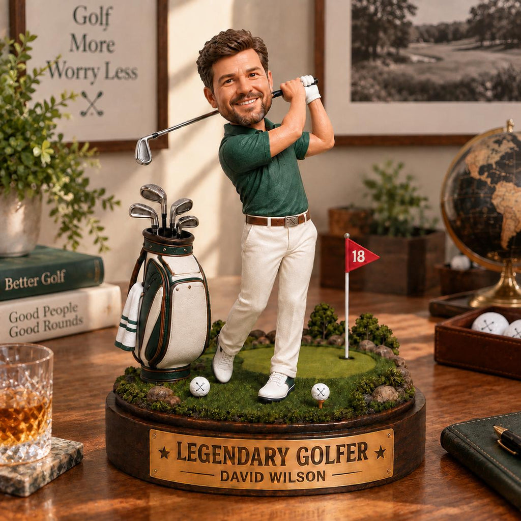 May include: A custom bobblehead figurine of a golfer wearing a green polo shirt and white trousers, swinging a golf club. The figure stands on a circular base with a golf bag, a red flag marked 18, and a brass plaque reading LEGENDARY GOLFER DAVID WILSON.