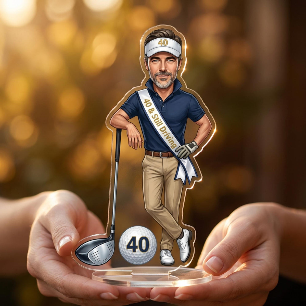 May include: A personalized acrylic golf-themed figurine featuring a cartoon man in a golf visor and polo shirt, holding a golf club. The figurine has a sash that reads "40 & Still Driving". A golf ball with the number "40" is also included.