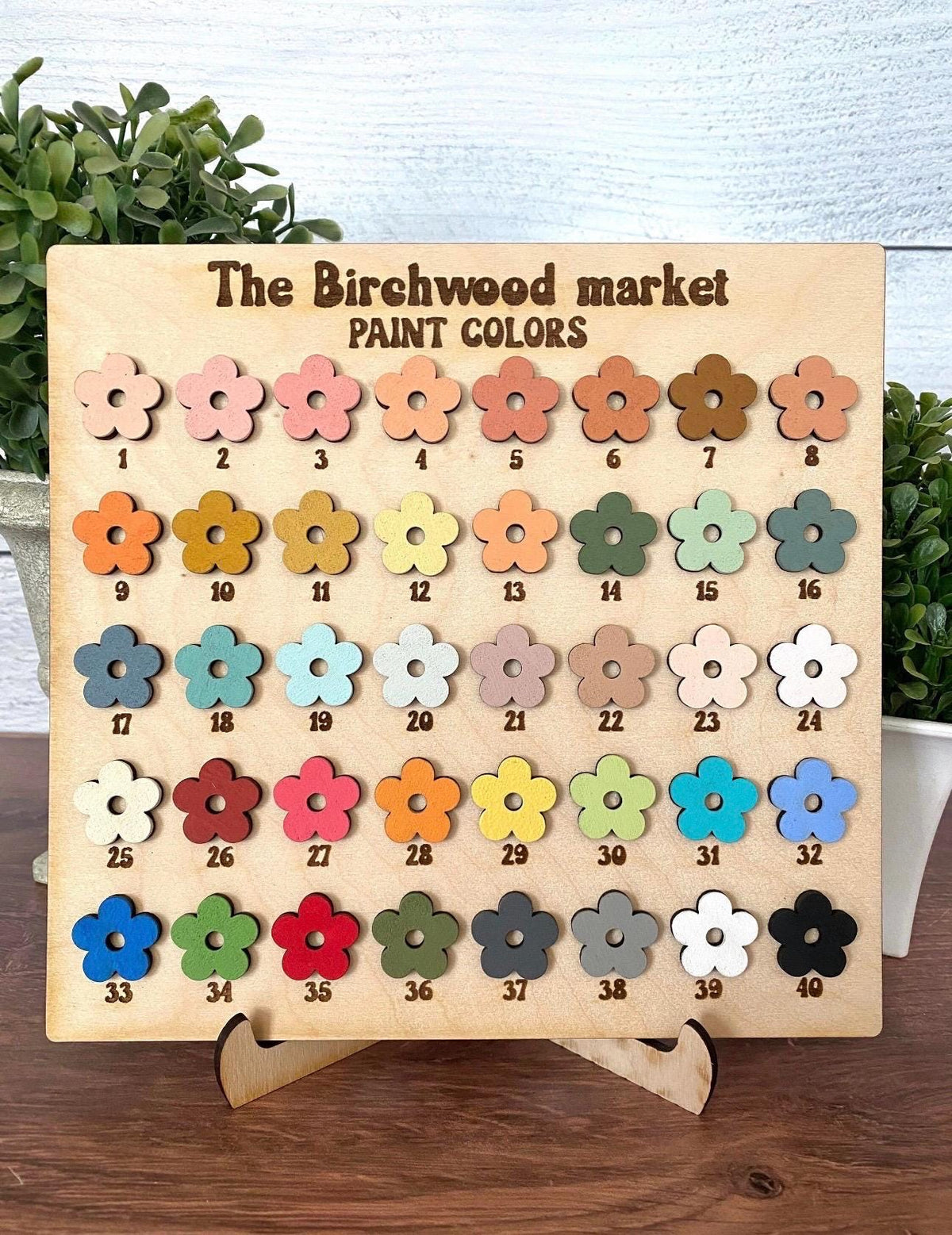 May include: A wooden display board with the text "The Birchwood market PAINT COLORS" and 40 flower-shaped paint color samples. The colors range from light pink to dark brown, with various shades of blue, green, and orange.