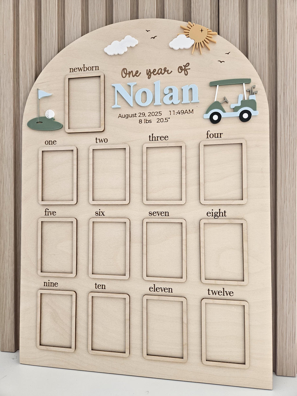 May include: An arched wooden milestone board featuring a golf theme with a green golf cart, a flag, and a sun. It includes a frame for a newborn photo and twelve frames labeled one through twelve, with text reading One year of Nolan, August 29, 2025, 11:49AM, 8 lbs 20.5 inches.