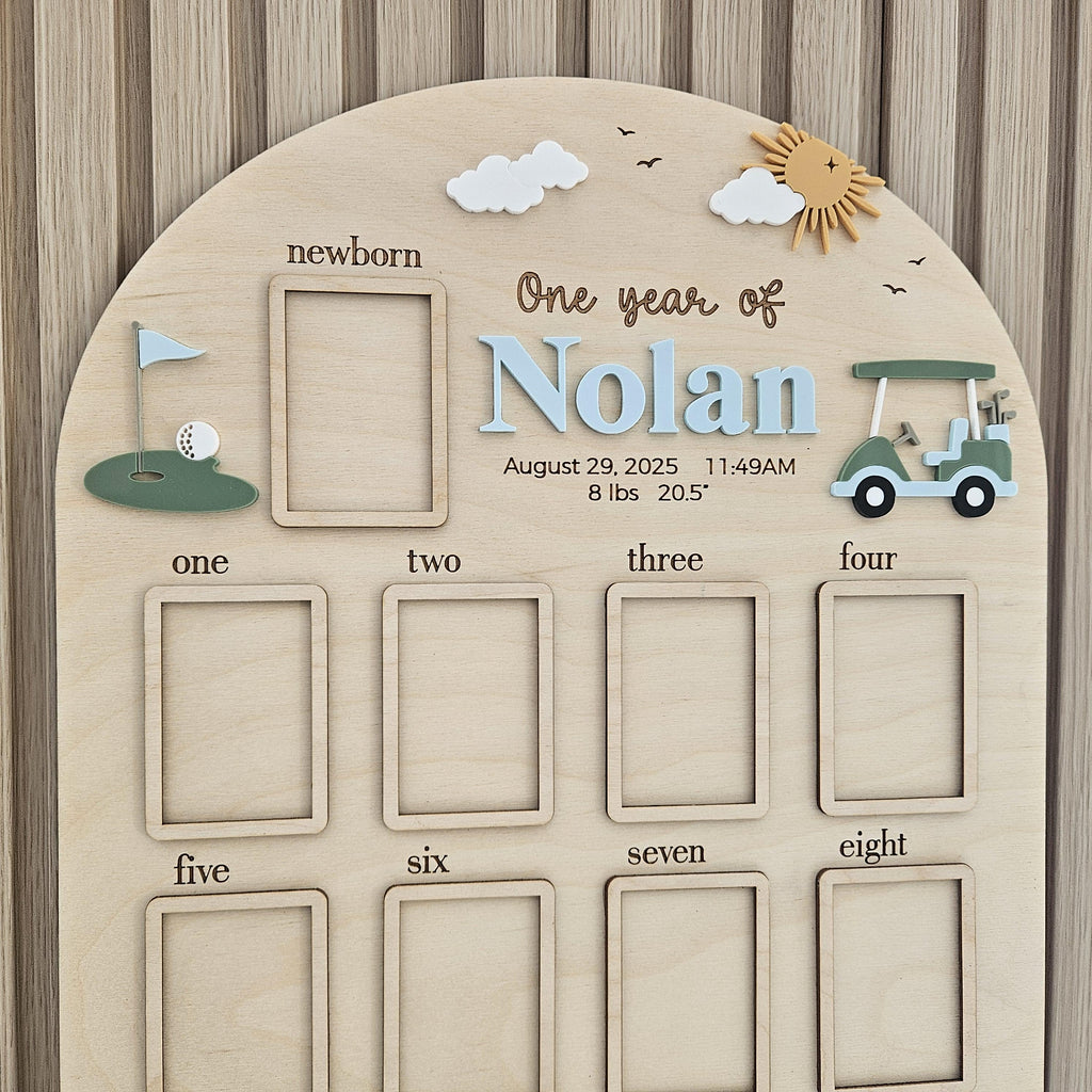 May include: An arched wooden baby milestone board featuring the name Nolan, a golf cart, and a golf hole graphic. It includes a newborn photo frame, text for birth details including 8 lbs and 20.5 inches, and eight additional photo frames.