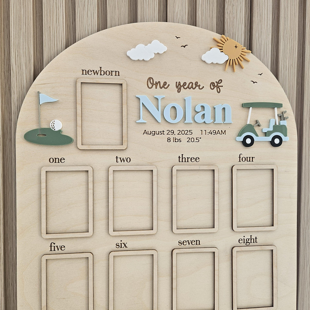 May include: An arched wooden baby milestone board featuring the name Nolan, a golf cart, and a golf hole graphic. It includes a newborn photo frame, text for birth details including 8 lbs and 20.5 inches, and eight additional photo frames.