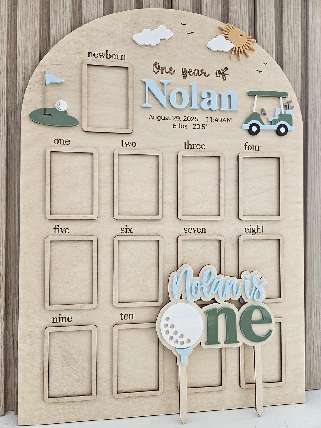 May include: An arched wooden milestone board featuring a golf theme with cutouts for photos from newborn to ten months. It displays the text One year of Nolan, August 29, 2025, 11:49AM, 8 lbs 20.5 inches, and includes a matching cake topper.