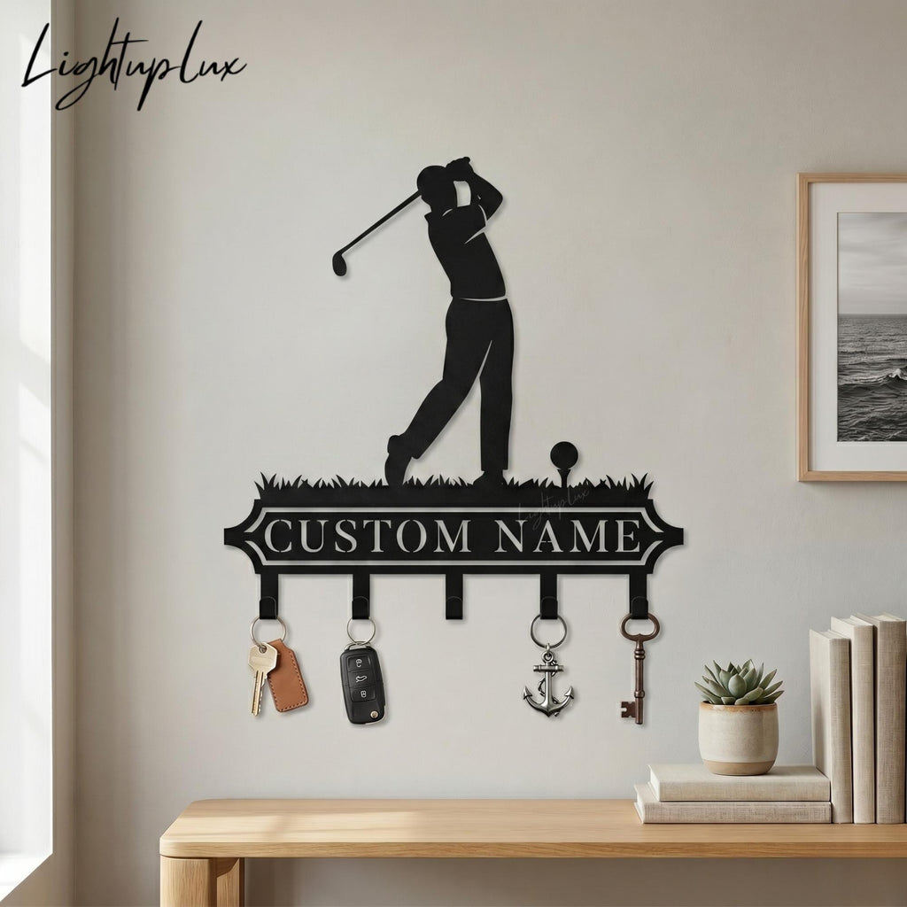 May include: Black metal key holder featuring a golfer silhouette, golf ball, and grass design. Includes hooks for keys and the text "CUSTOM NAME". The key holder has keys, a car key fob, and an anchor keychain hanging from the hooks.