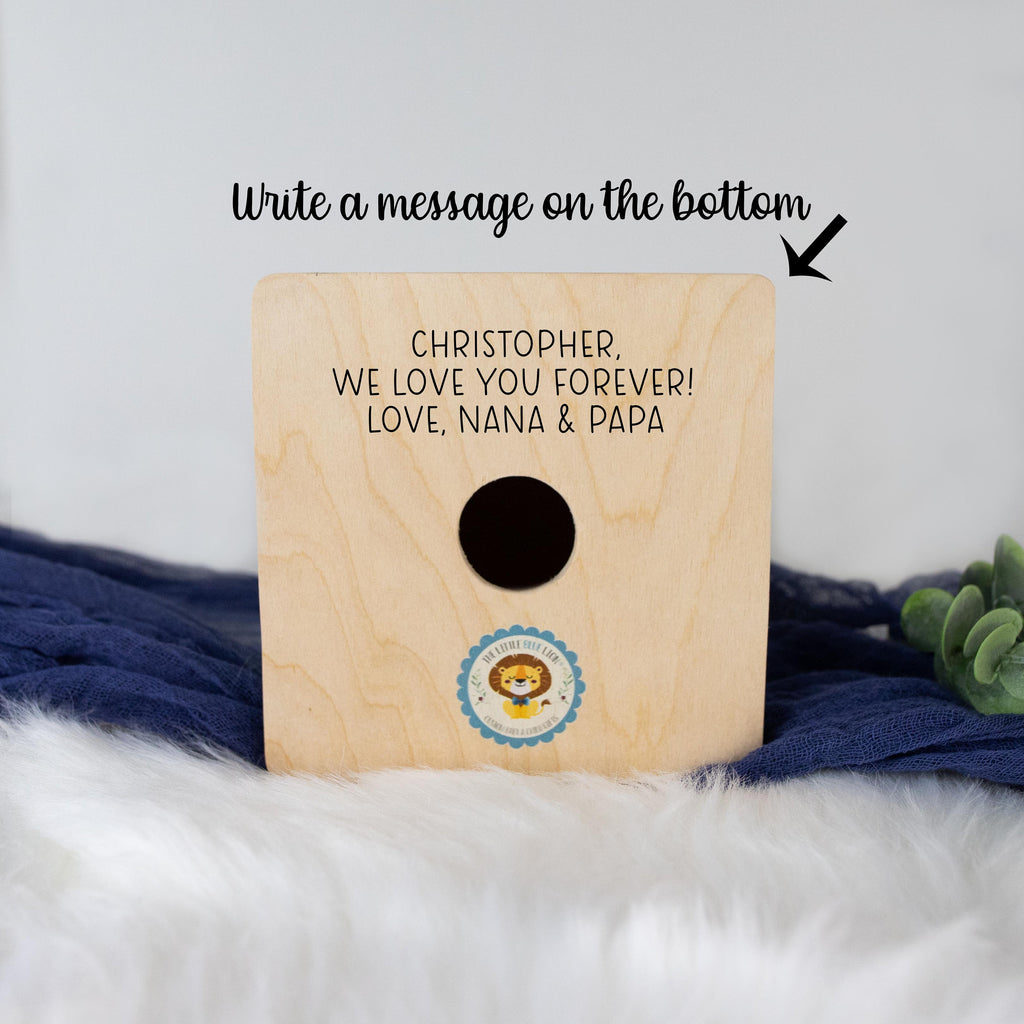 May include: A wooden box with a cutout for a photo or other keepsake. The box is decorated with a lion illustration and the text "The Little Lion King". The text "CHRISTOPHER, WE LOVE YOU FOREVER! LOVE, NANA & PAPA" is written on the front of the box.
