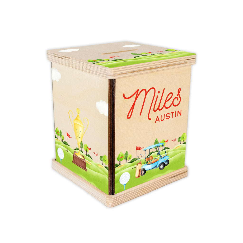 May include: A wooden golf-themed money box with a green, brown, and blue design. The box has a slot on the top for coins and a personalized inscription that reads "Miles AUSTIN".