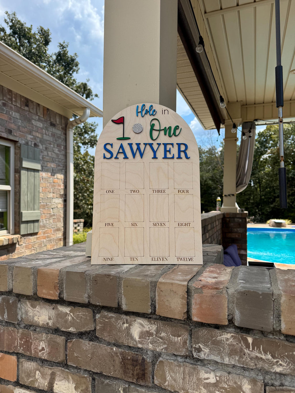 May include: Wooden golf-themed sign with the text "Hole in One SAWYER". The sign has a golf ball and flag graphic. It includes spaces for tracking scores from one to twelve.