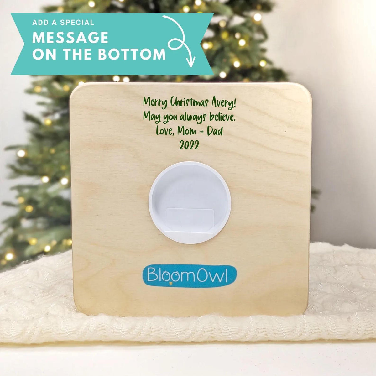 a wooden plaque with a message on it, placed on a white surface in front of a Christmas tree.