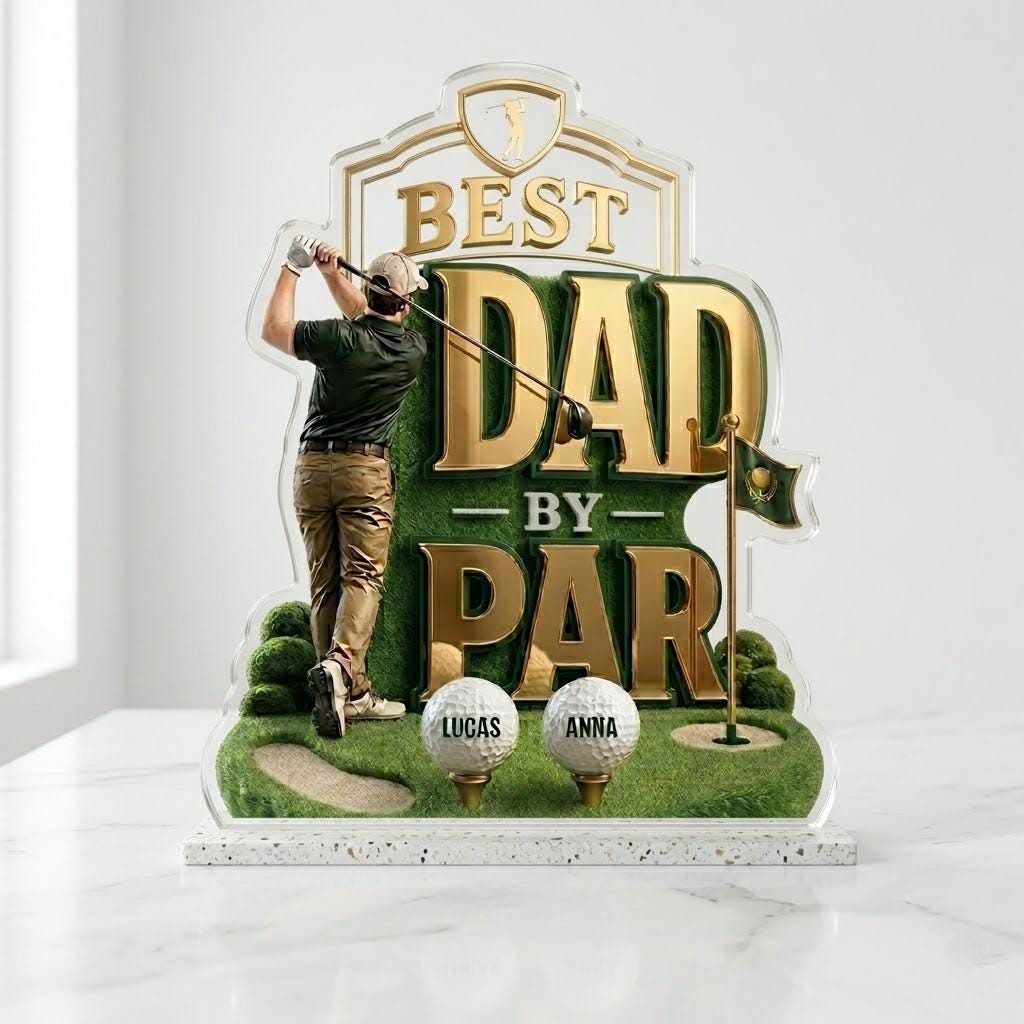 May include: A decorative golf-themed sign with the text "BEST DAD BY PAR" in gold. It features a golfer figurine, golf balls with names, and a small flag. The base is a speckled white, and the overall design is a gift for golf enthusiasts.