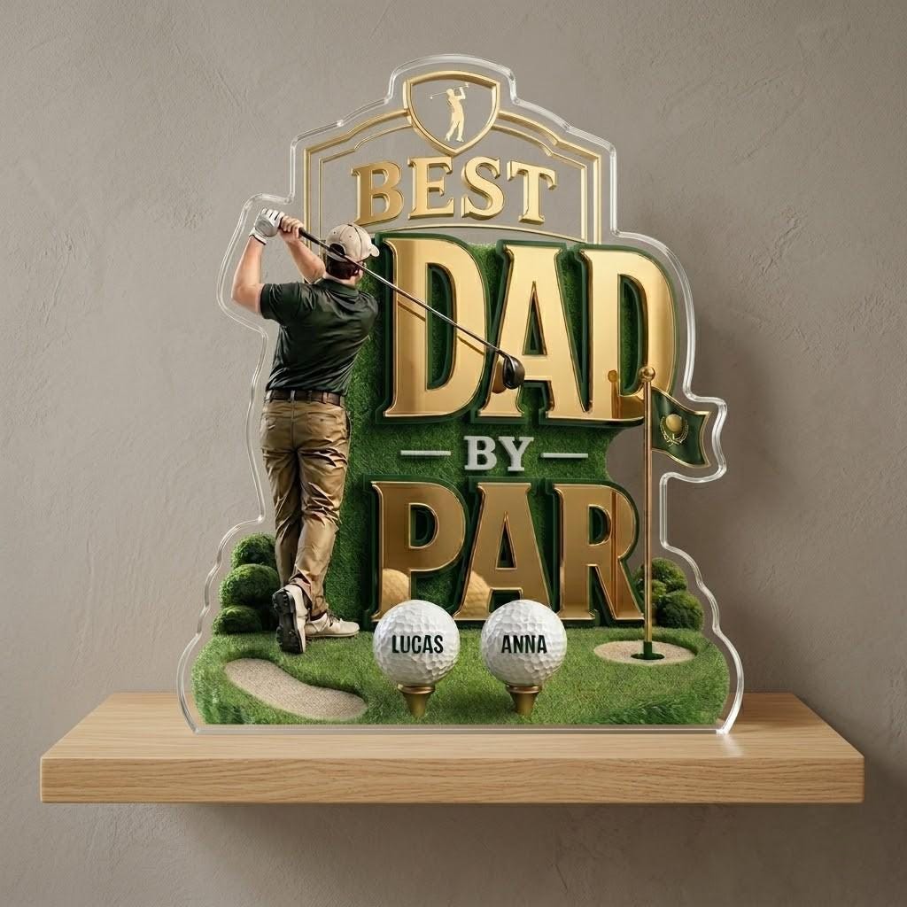May include: A golf-themed acrylic plaque with the words "BEST DAD BY PAR" in gold lettering. The design includes a golfer, golf balls, and a green golf course scene. The names "Lucas" and "Anna" are printed on the golf balls.
