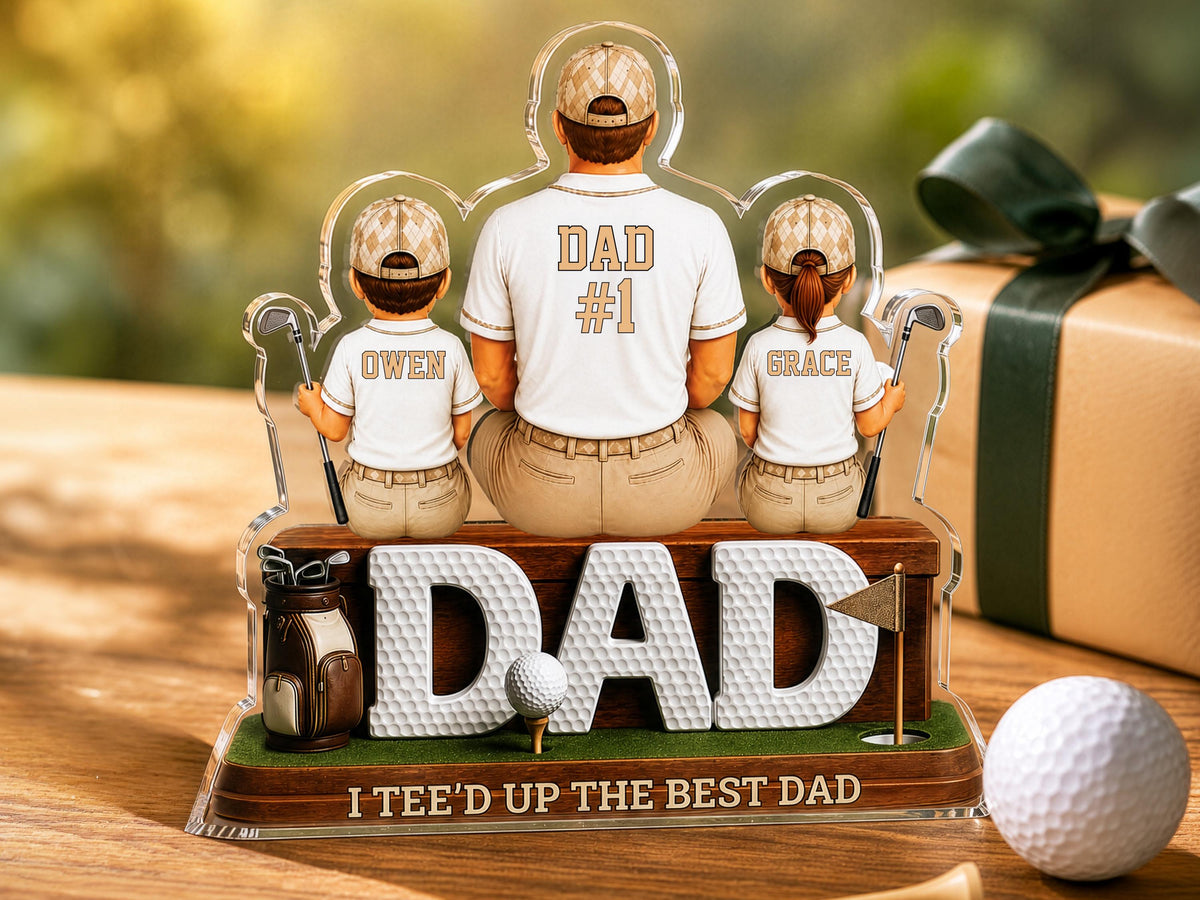 May include: A clear acrylic display featuring a central figure labeled DAD #1 flanked by two smaller figures labeled OWEN and GRACE, all wearing golf attire. The base is wood-toned with the text DAD and I TEE'D UP THE BEST DAD in white.