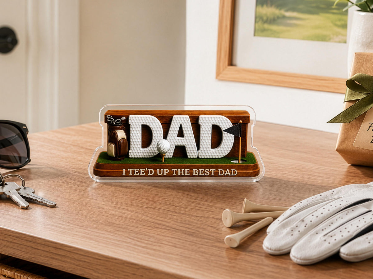 May include: A decorative desk sign featuring the word DAD in white, textured golf ball-style lettering. The base is brown wood with green turf, a miniature golf bag, a golf ball on a tee, a black flag, and the text I TEE'D UP THE BEST DAD.