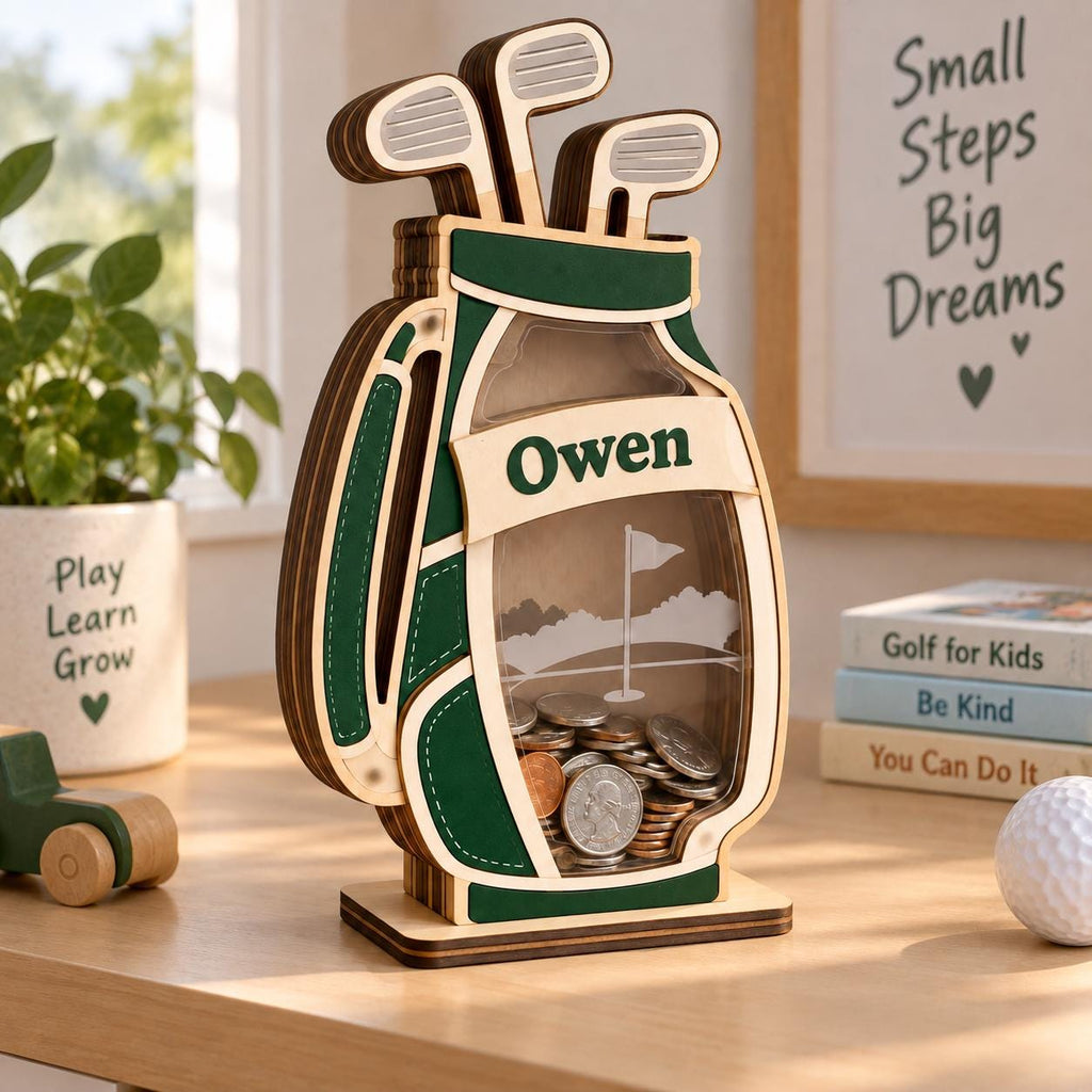 May include: A wooden golf bag-shaped piggy bank with a clear front panel, featuring the name Owen printed on a banner. The design includes three golf clubs at the top and a golf course graphic on the back panel, filled with various metal coins.