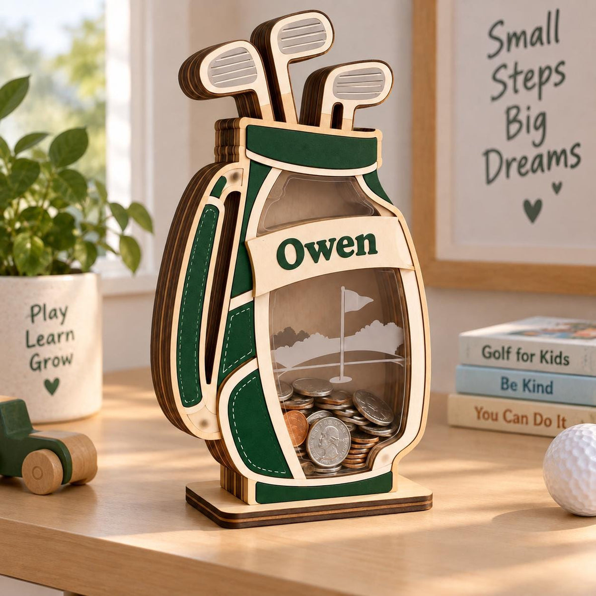 May include: A wooden golf bag-shaped piggy bank with a clear front panel, featuring the name Owen printed on a banner. The design includes three golf clubs at the top and a golf course graphic on the back panel, filled with various metal coins.