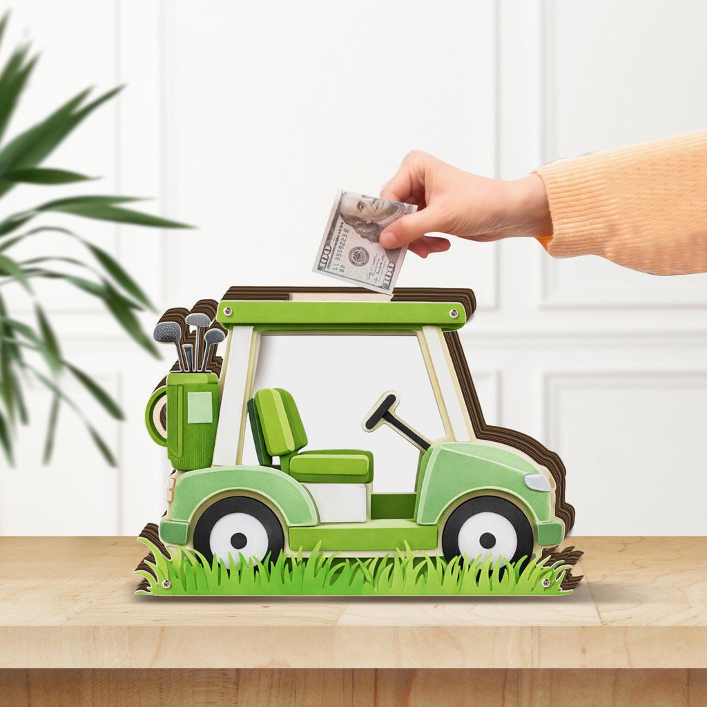 May include: A green and white wooden golf cart-shaped bank with a brown outline. The bank has a seat, steering wheel, and golf club bag. A hand is inserting a one hundred dollar bill into the slot on top. The bank sits on a wooden surface.