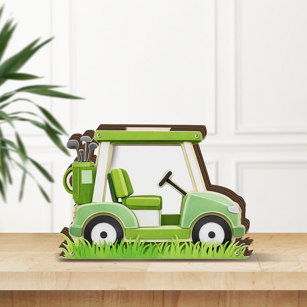 May include: A decorative wooden golf cart in shades of green, brown, and white. The cart features a steering wheel, seat, and a golf bag with clubs. The base includes cut-out grass, and the cart is displayed on a wooden surface.