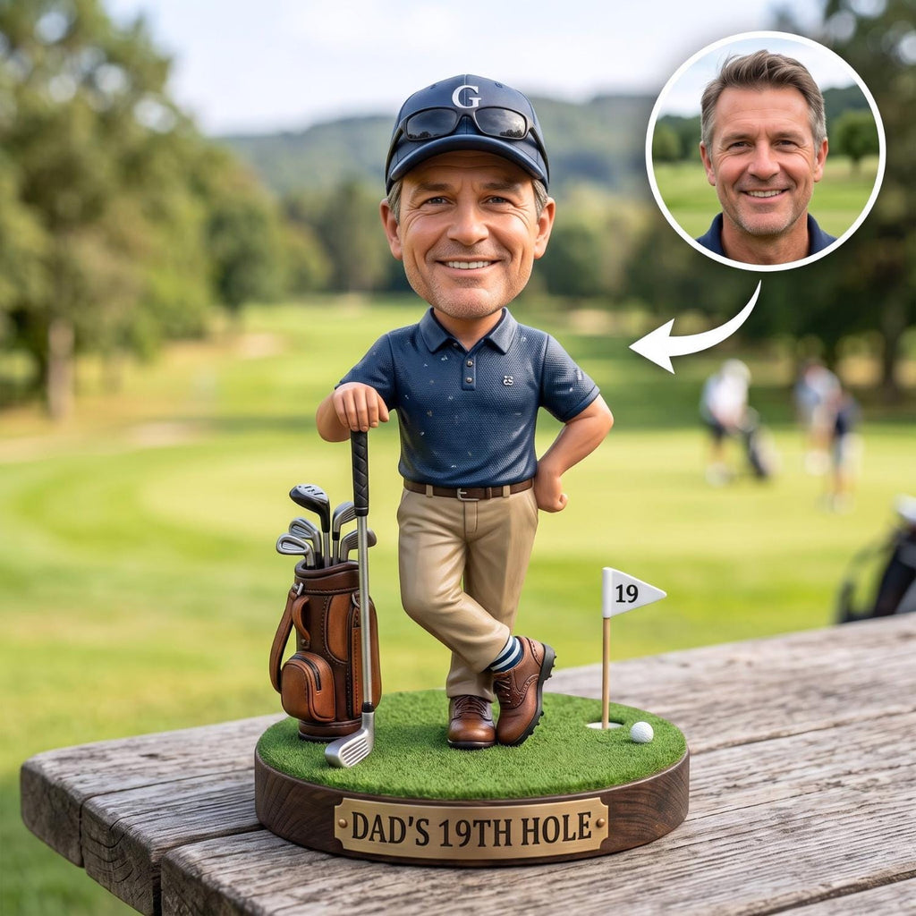 May include: A custom bobblehead figurine of a smiling golfer wearing a navy blue polo shirt, tan trousers, and a navy cap with sunglasses. The figure stands on a green base with a golf bag, a club, a flag labeled 19, and a plaque reading DAD'S 19TH HOLE.