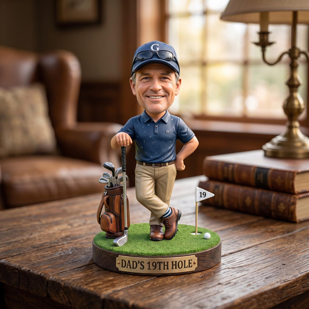 May include: A bobblehead figure of a smiling golfer wearing a navy blue polo shirt, khaki pants, and a navy cap with a white G. The figure stands on a green base with a golf bag, a club, a flag labeled 19, and a plaque reading DAD'S 19TH HOLE.