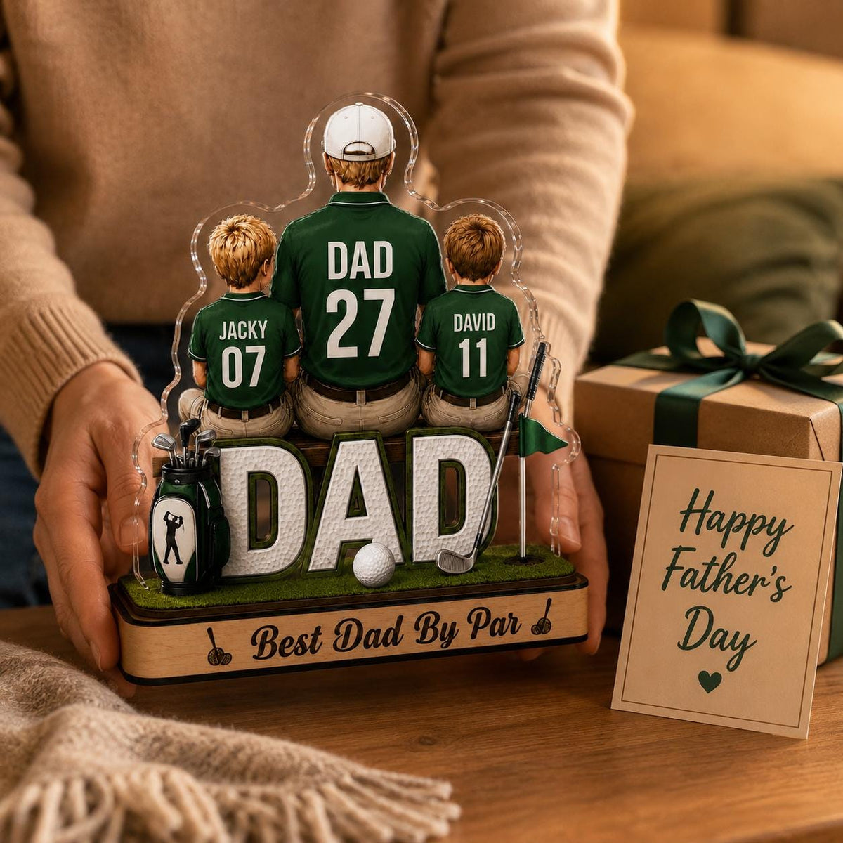 May include: A personalized golf-themed Father's Day gift. The acrylic display features a father and two sons in golf attire, with the word "DAD" prominently displayed. Includes a golf ball, golf bag, and the text "Best Dad By Par."