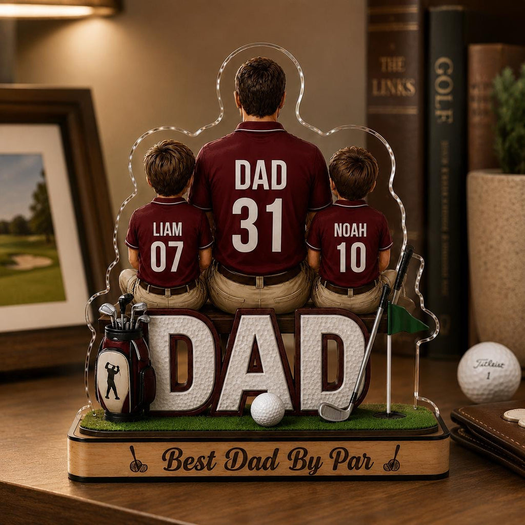 May include: A decorative golf-themed acrylic figurine featuring a father and two sons, with the word "DAD" prominently displayed. The sons' shirts have the names "Liam" and "Noah" with numbers. A golf ball and clubs are also included. The base reads "Best Dad By Par."