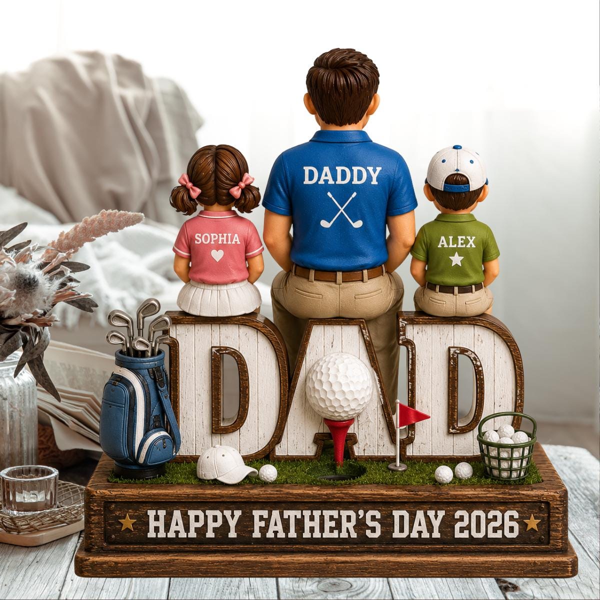 May include: A Father's Day golf-themed figurine with the word "DAD" in large letters. The figurine features a father figure with two children, a golf bag, golf balls, and the text "HAPPY FATHER'S DAY 2026".
