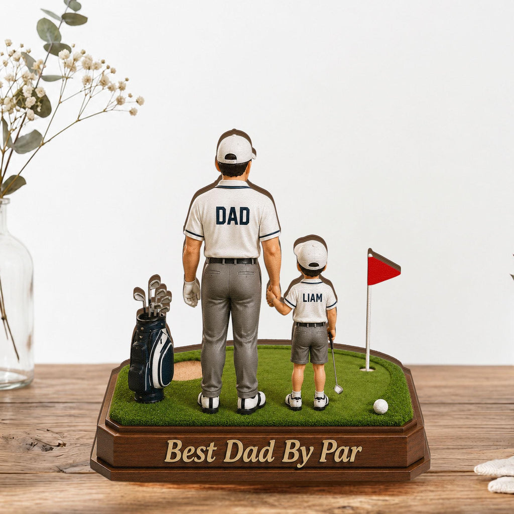 May include: A golf-themed figurine featuring a father and child holding hands on a miniature green. The father's shirt reads "DAD," and the child's reads "LIAM." A golf bag, flag, and the text "Best Dad By Par" are also present.