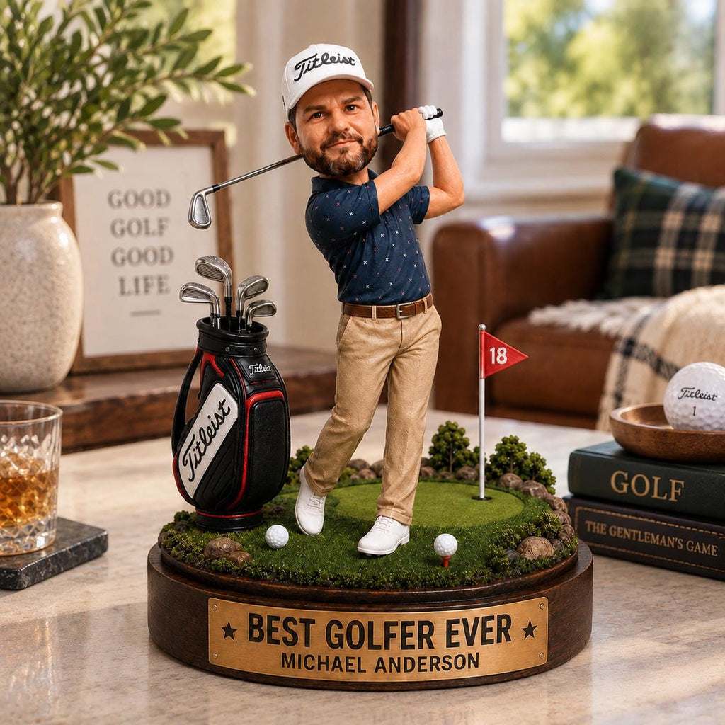 May include: A custom bobblehead figurine of a golfer wearing a white Titleist cap, navy patterned polo, and khaki pants, swinging a club. The figure stands on a circular base with a green putting surface, a golf bag, and a plaque reading BEST GOLFER EVER.