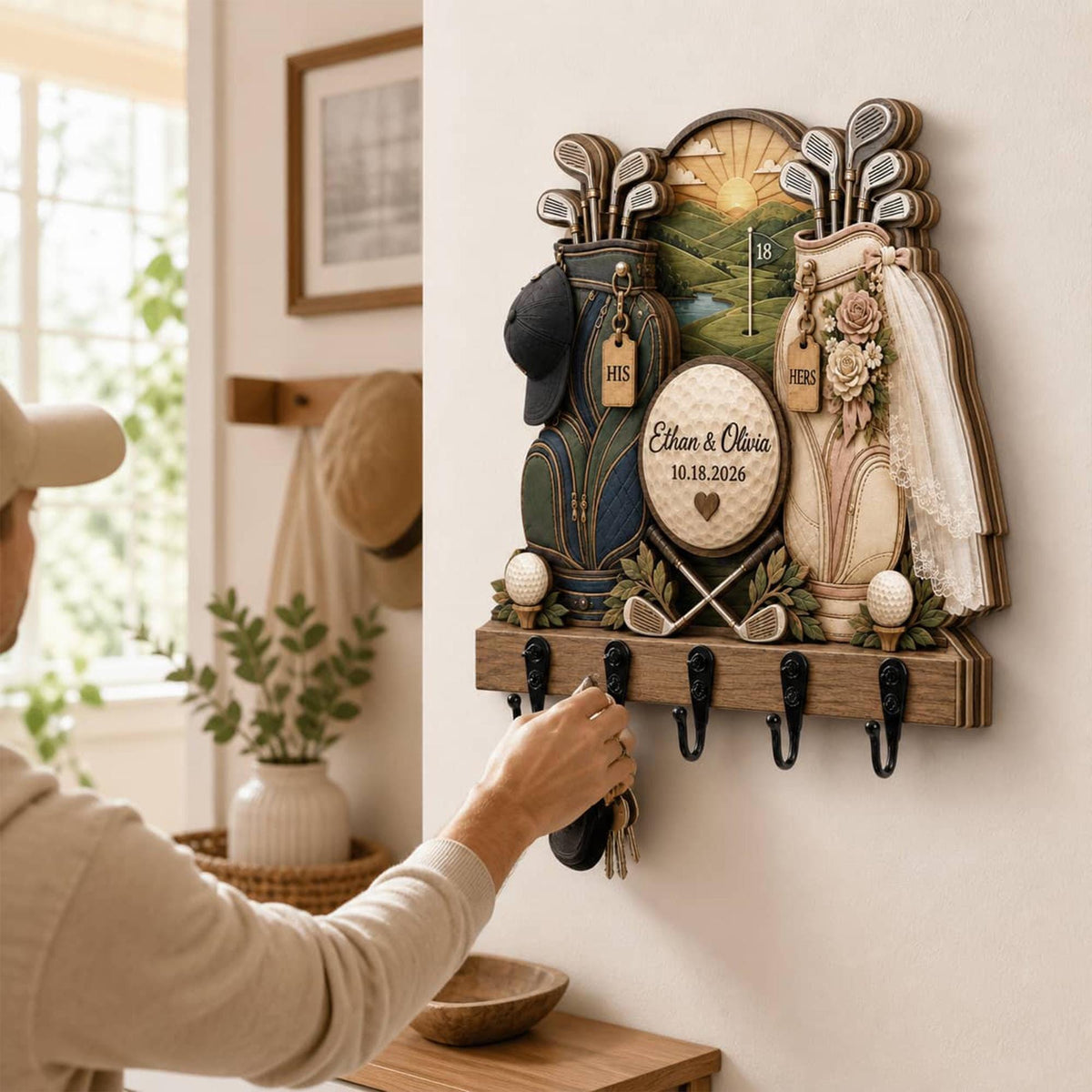 May include: A wall-mounted wooden key holder featuring a layered golf-themed design with two golf bags, a central golf ball with the text Ethan & Olivia 10.18.2026, a golf course background, and five black metal hooks for hanging keys.