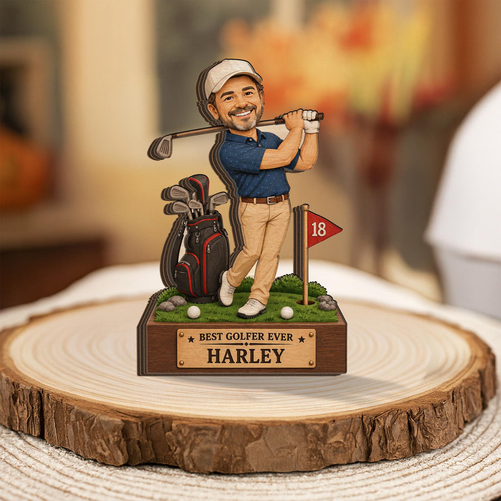 May include: A layered wooden figurine of a golfer wearing a blue polo shirt and tan pants, holding a golf club. Beside the figure is a black golf bag, a red flag with the number 18, and two golf balls. A plaque reads BEST GOLFER EVER HARLEY.