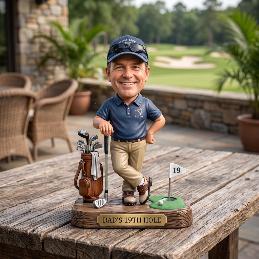 May include: A bobblehead figurine of a golfer wearing a navy blue polo shirt, khaki pants, and a navy blue cap with sunglasses. The figure stands on a base labeled DAD'S 19TH HOLE, featuring a golf bag with clubs, a golf ball, and a flag marked 19.