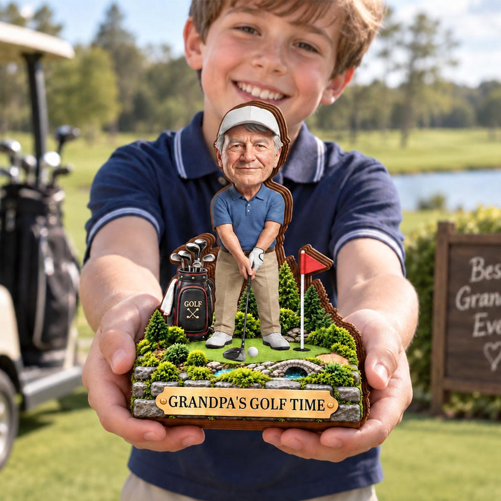 May include: A custom bobblehead figurine featuring a golfer in a blue polo shirt and khaki pants, standing on a miniature golf course base with a golf bag, flag, and stone bridge, with a plaque reading GRANDPA'S GOLF TIME at the front.