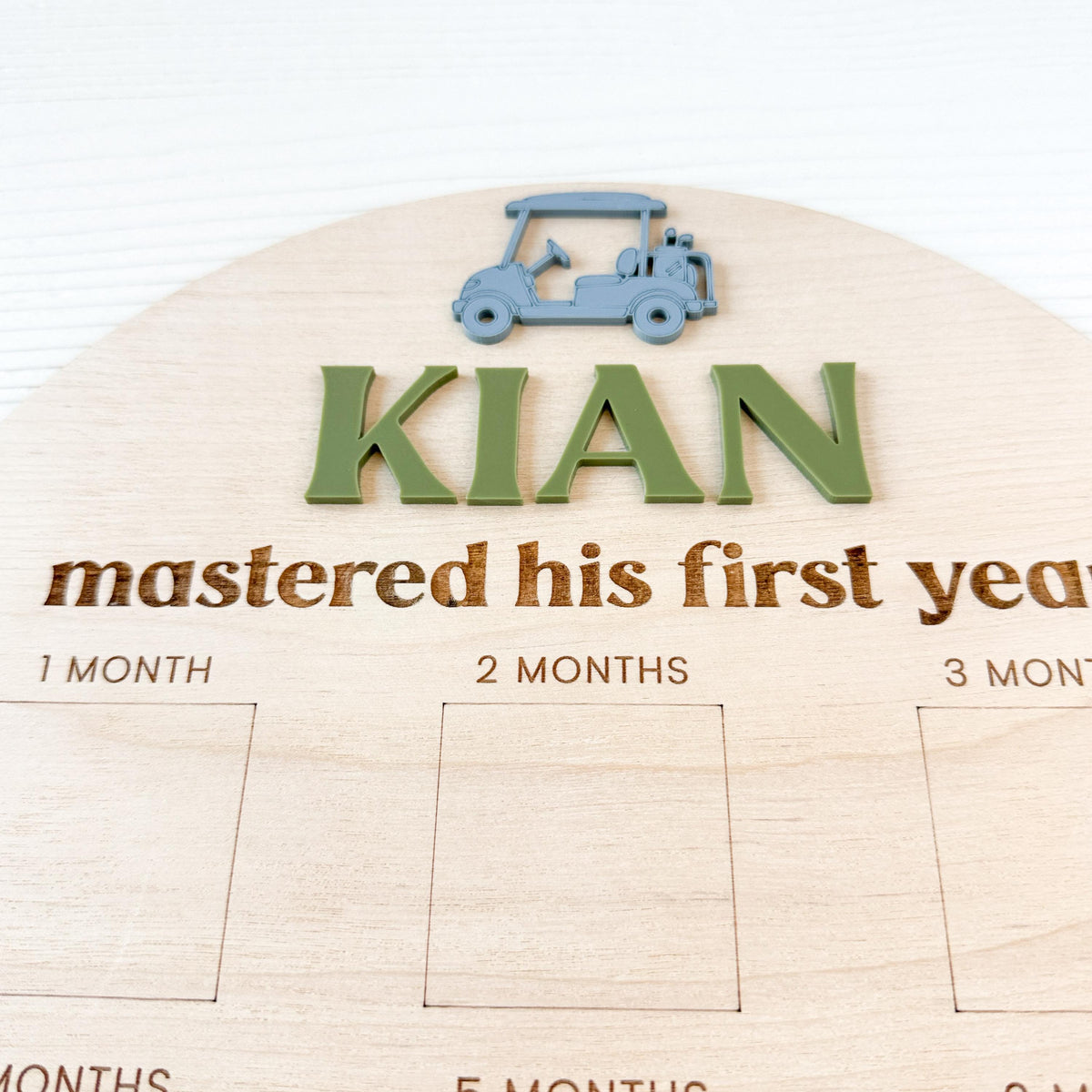 close-up of custom acrylic name and golf cart accent on wood milestone photo board.  detailed view of engraved elements for baby’s first birthday keepsake